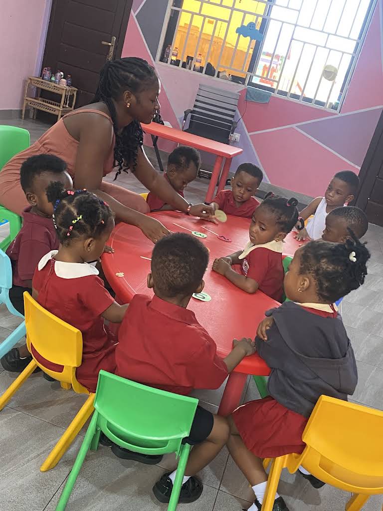 An ALLSWELL Premier School teacher guiding early-years learners around a classroom table