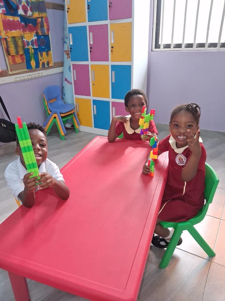 Three young ALLSWELL Premier School learners smiling and showing the colourful models they built